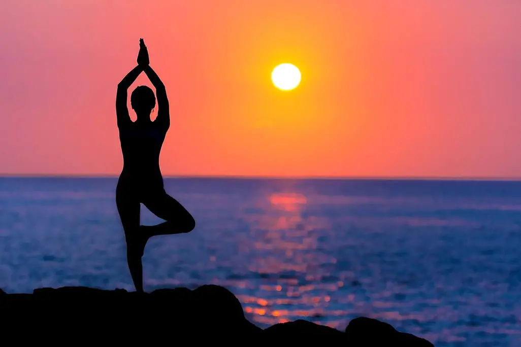 Silhouette of a person in the yoga-tree pose in front of the ocean at sunset.